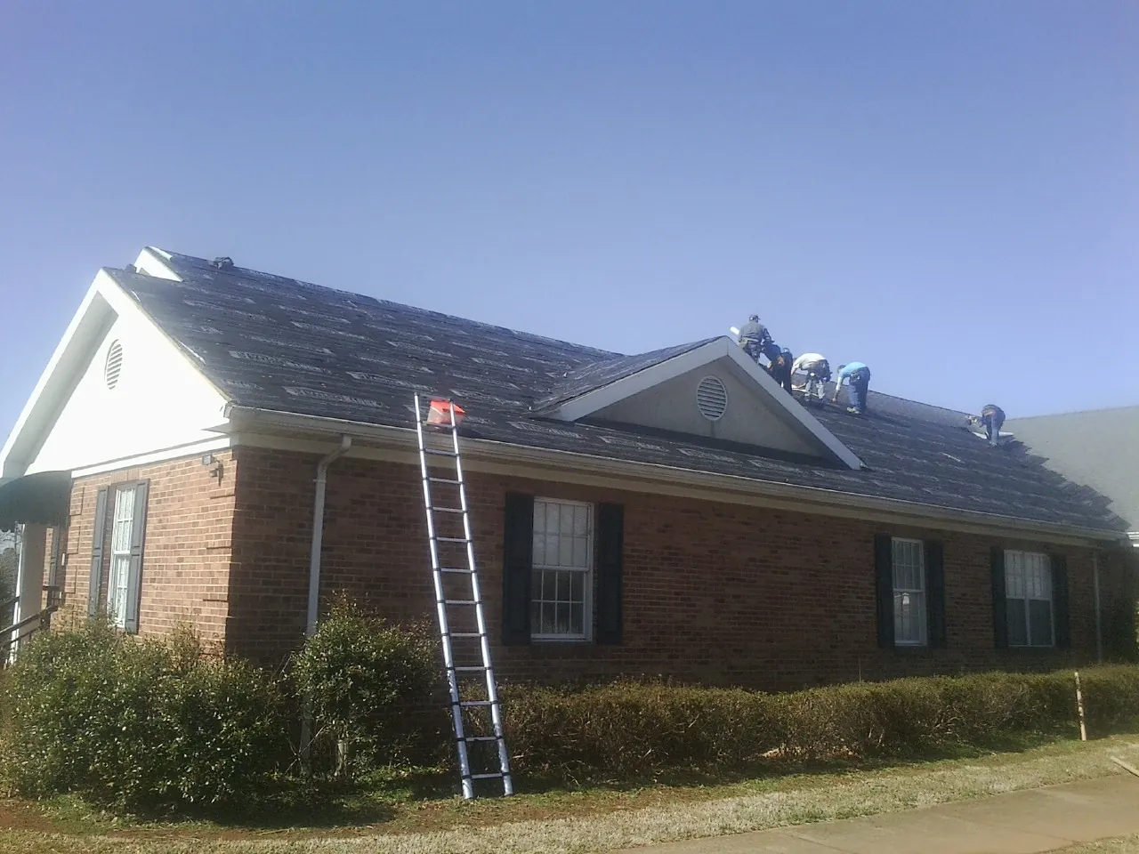 Crew tearing shingles off a brick ranch roof with a ladder set — Emergency Roof Repair work by our crew in Randolph